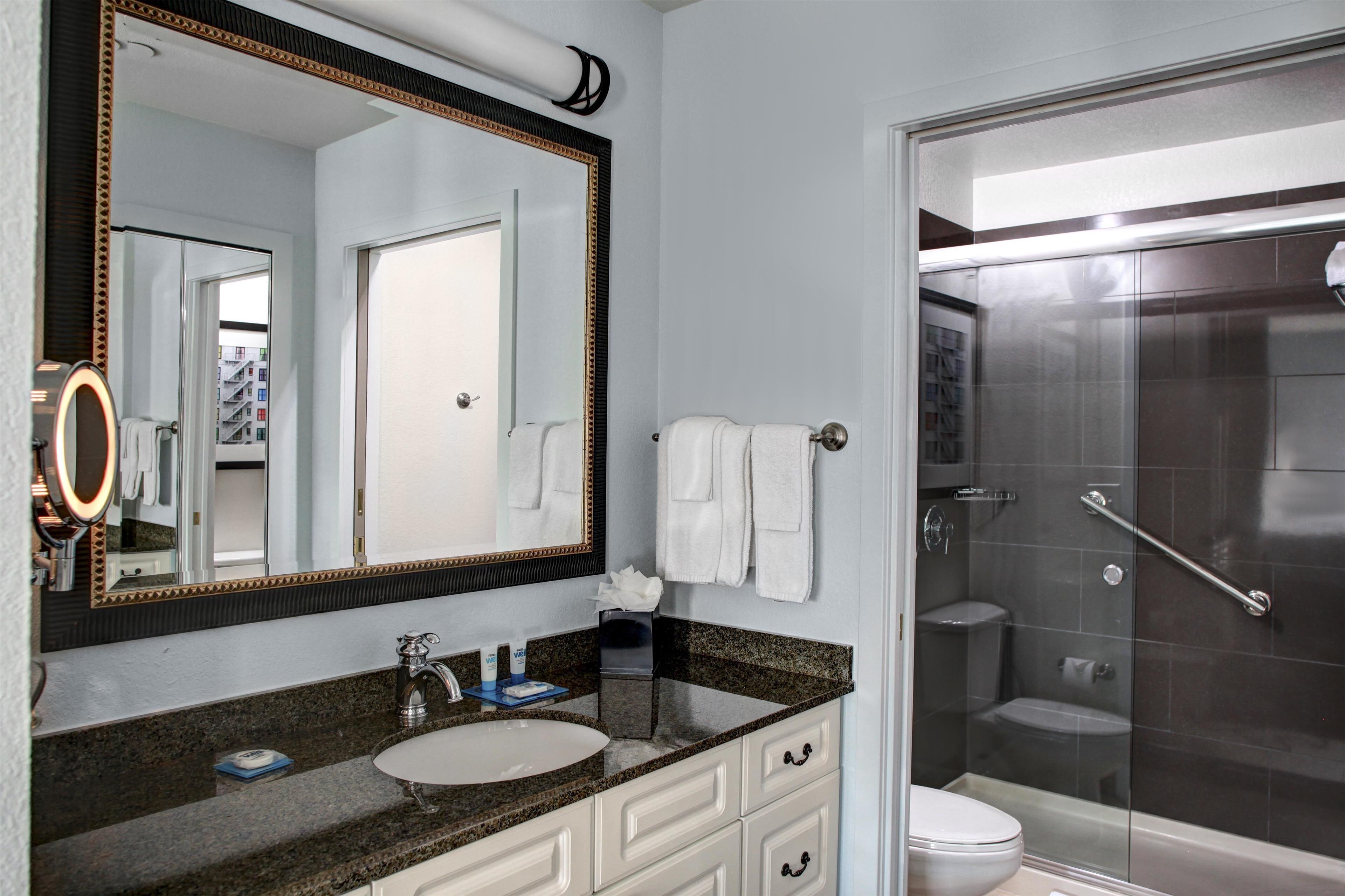 A bathroom with a large mirror, a sink, a toilet, and a shower.
