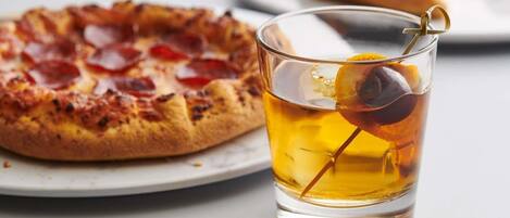 A pizza with pepperoni and a glass of beer with an olive.