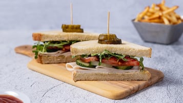 Two sandwiches with toothpicks on a wooden board, a bowl of fries, and a small bowl of ketchup.