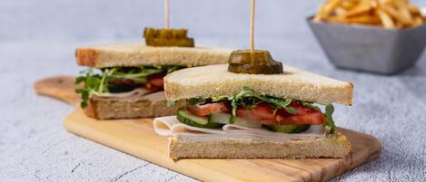 Dos sándwiches con palillos en una tabla de madera, un bol de papas fritas y un pequeño bol de kétchup.