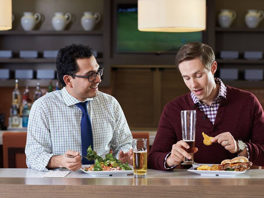 Dos hombres cenando en un restaurante, mesa para dos, una copa de cerveza y un plato de comida.