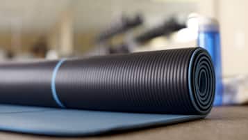 Een yogamat en een opgerolde yogamat op een houten ondergrond.