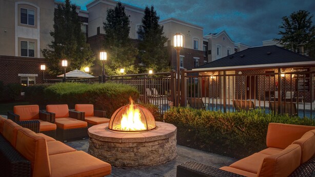 An outdoor patio with a stone fire pit, orange cushioned seating, and a pool area.
