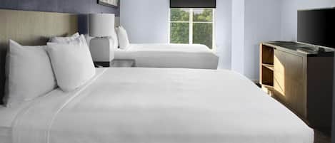 A hotel room with two beds, a TV, a desk, and a window with a view of trees.