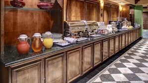 A buffet counter with various food and drink options, wooden cabinets, and a checkered floor.
