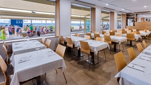 A restaurant with multiple tables and chairs, large windows offering a view of the beach, and a sign for the beach bar. - 4R Miramar Calafell (Calafell)