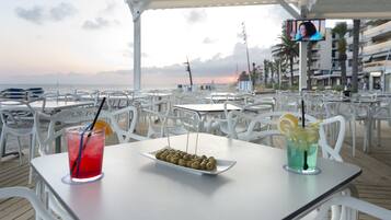 A beachside restaurant with outdoor seating, a view of the ocean, and a television screen.
