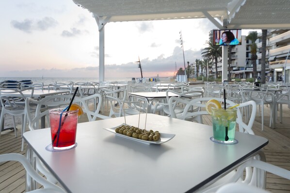 Un restaurante frente a la playa con terraza, vistas al océano y una pantalla de televisión.