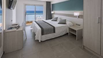 A modern hotel room with a large bed, bedside tables, a desk with a chair, and a view of the sea through a sliding glass door.