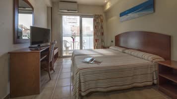 Habitación de hotel con cama, escritorio con computadora, silla, balcón con mesa y sillas, y un cuadro en la pared.