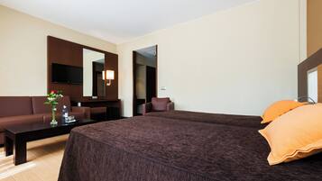 A hotel room with a large bed, a sofa, a coffee table, a TV, and a bathroom visible through an open door.