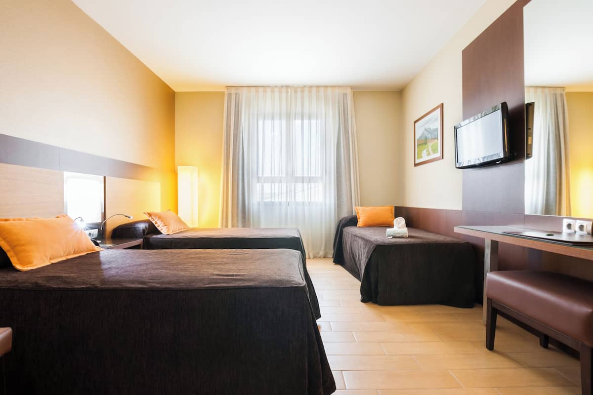 Ein Hotelzimmer mit zwei Betten, einem Schreibtisch, einem Fernseher und einem großen Fenster mit Vorhängen.