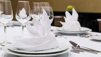 Una mesa dispuesta con platos blancos, cubiertos y copas de vino transparentes.