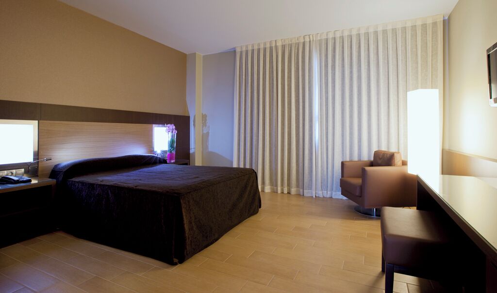 A hotel room with a bed, a desk, a chair, and a large window with curtains.