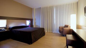 A hotel room with a bed, a desk, a chair, and a large window with curtains.