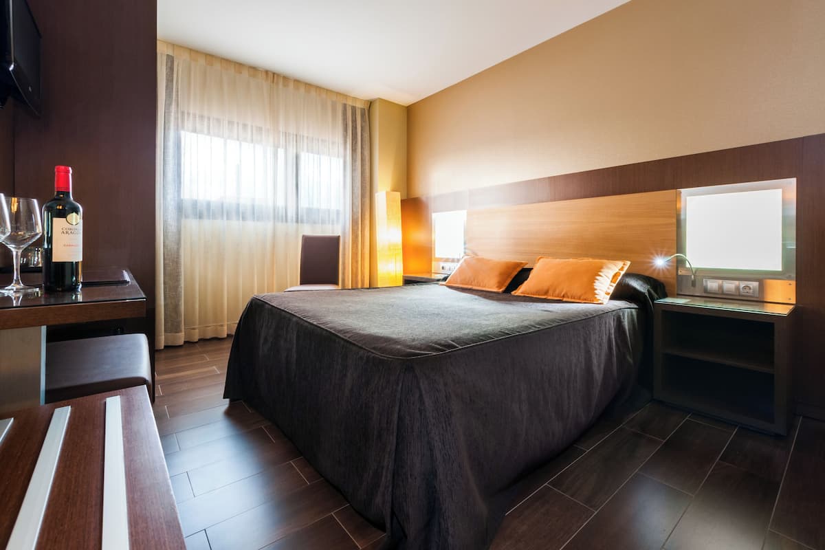 Ein Hotelzimmer mit einem großen Bett, einem Schreibtisch mit einer Weinflasche und einer Lampe.