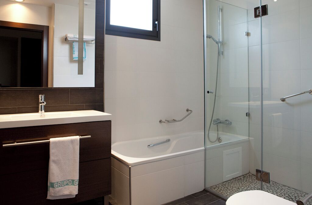 A modern bathroom with a glass-enclosed shower, a white bathtub, and a vanity with a towel hanging.