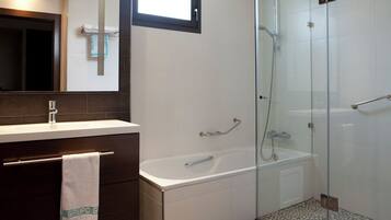 A modern bathroom with a glass-enclosed shower, a white bathtub, and a vanity with a towel hanging.