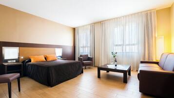 Een hotelkamer met een bed, twee stoelen, een salontafel en een bureau met een lamp.