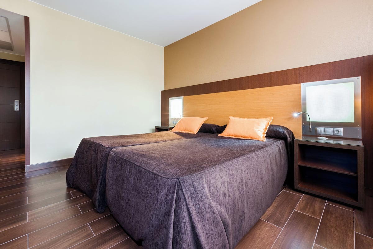 Ein modernes Hotelzimmer mit einem großen Bett, zwei Nachttischen und einem integrierten Fernseher.