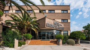 A hotel with a brick facade, a palm tree in the foreground, and a clear sky.
