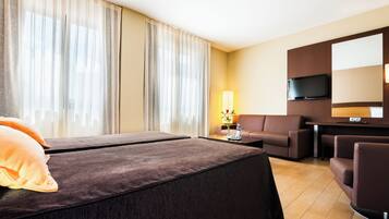 A hotel room with a bed, a sofa, a TV, and a lamp.