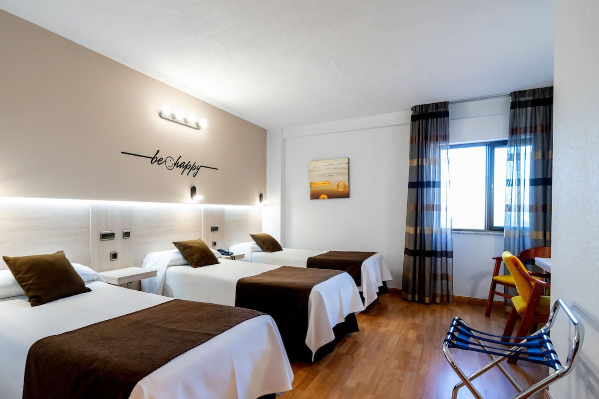Une chambre d’hôtel avec quatre lits, un bureau, une chaise et une fenêtre avec des rideaux.