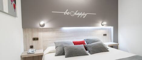 A modern hotel room with a bed, bedside tables, a phone, and a wall with a 'be happy' sign.