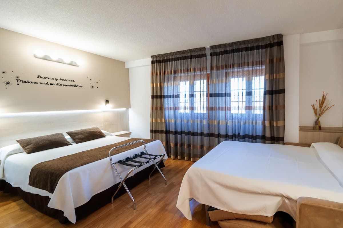 Une chambre d’hôtel avec deux lits, un plancher en bois, un téléviseur à écran plat et une fenêtre avec des rideaux à rayures.