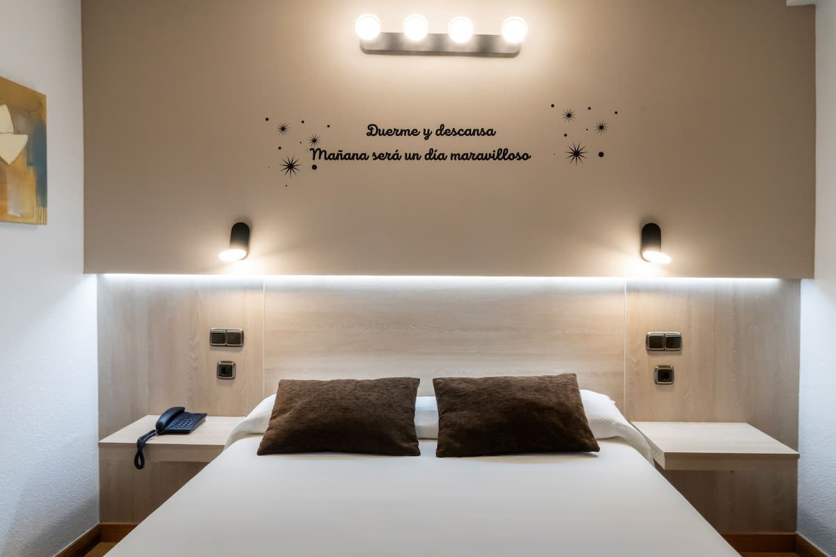 Une chambre d’hôtel avec un grand lit, deux tables de chevet, un téléphone et un mur orné d’une citation inspirante.