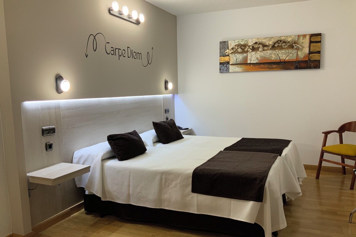 A neatly arranged hotel room with a large bed, bedside tables, a wall-mounted light fixture, and a painting.