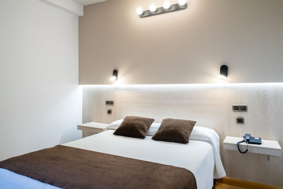 Un lit bien fait, avec une couverture marron et des oreillers, des tables de chevet avec des lampes et un téléphone posé sur une étagère.