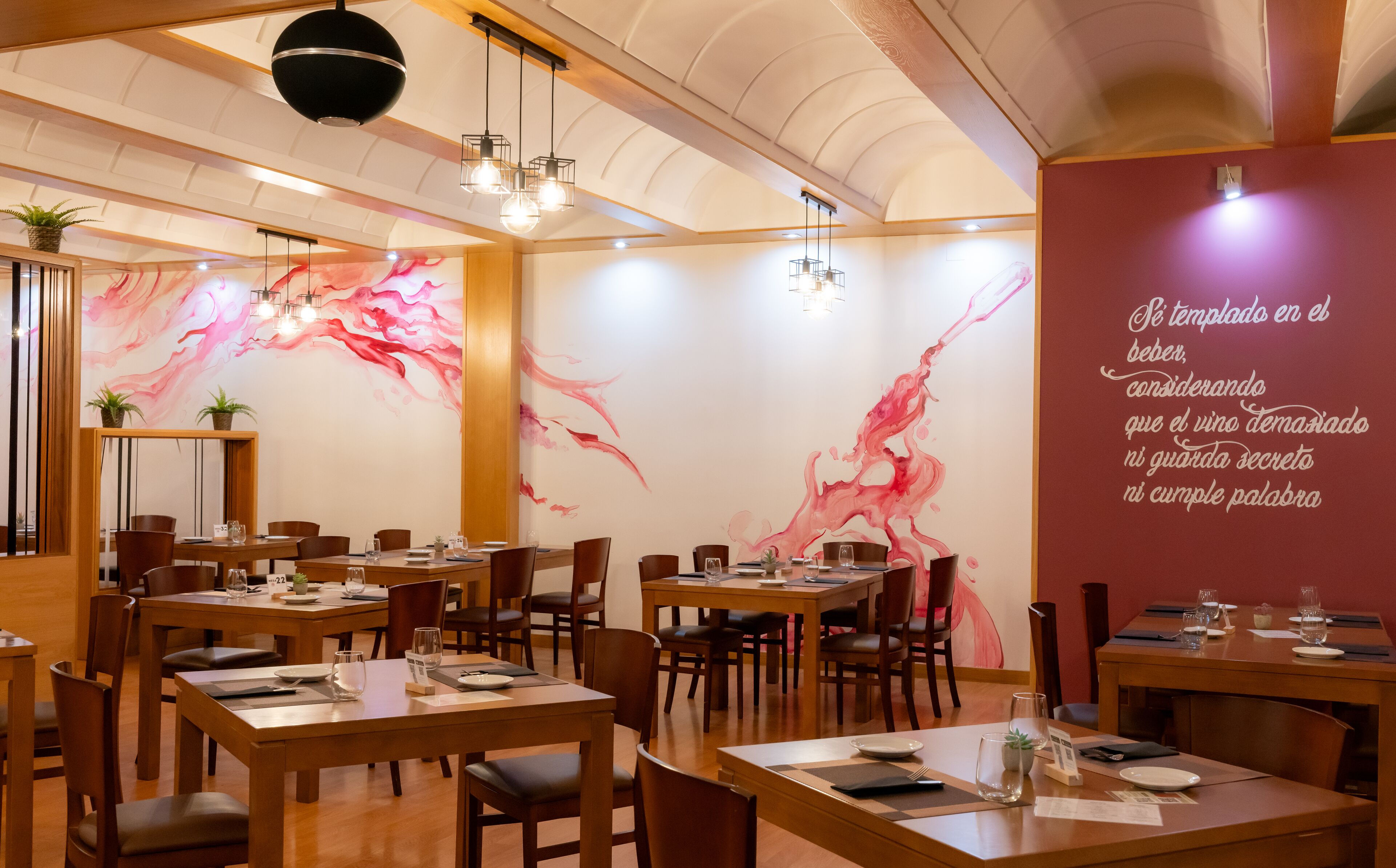 A restaurant with wooden tables and chairs, a marble wall with pink abstract art, and hanging pendant lights.