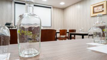 A conference room with a wooden table, clear glass bottles, and a projector screen in the background.
