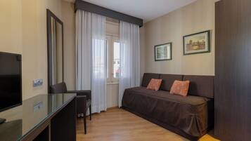 A modern hotel room with a glass desk, a brown sofa, and a large mirror.