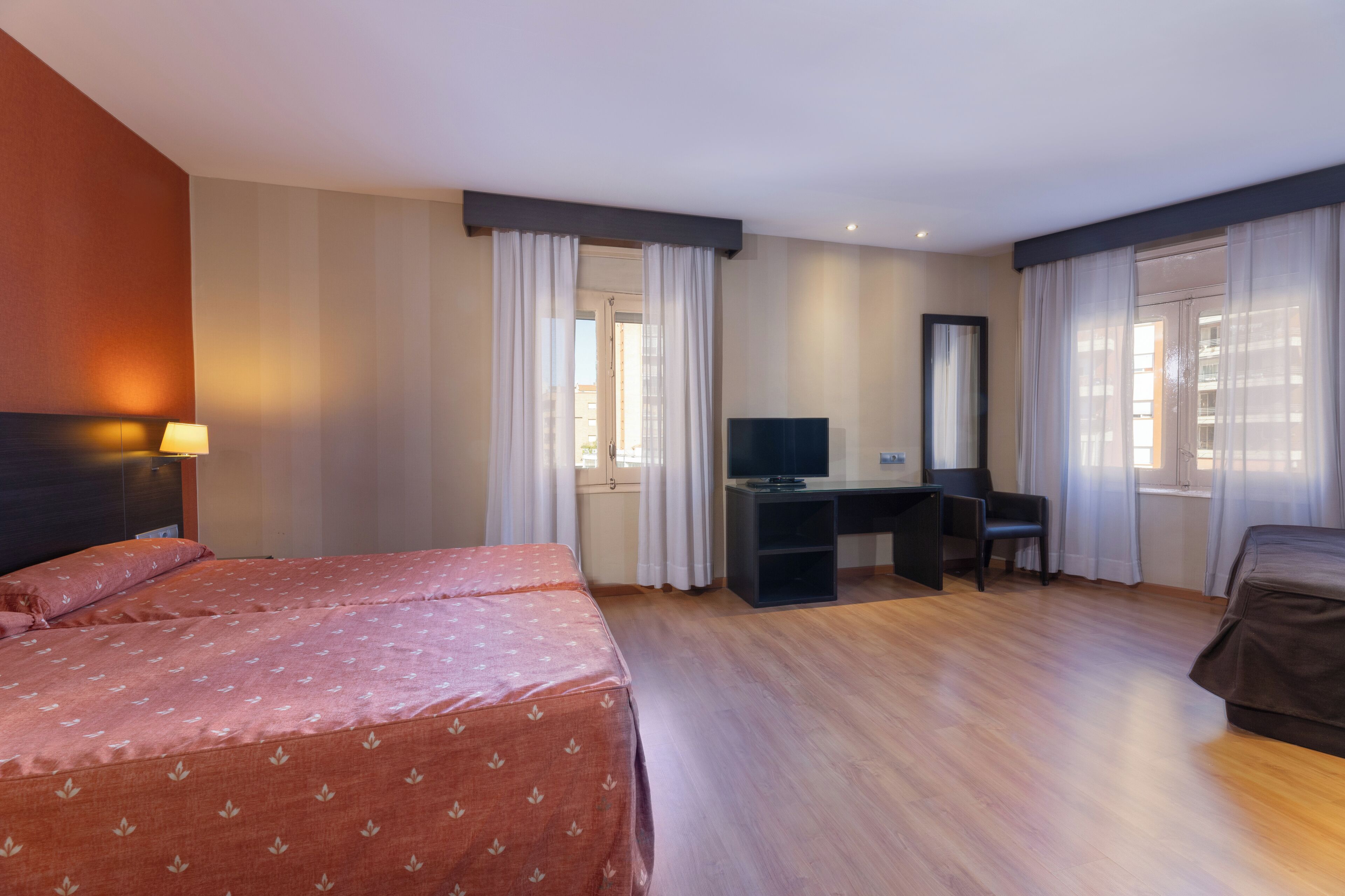 A hotel room with two beds, a desk, a chair, a television, and curtains.