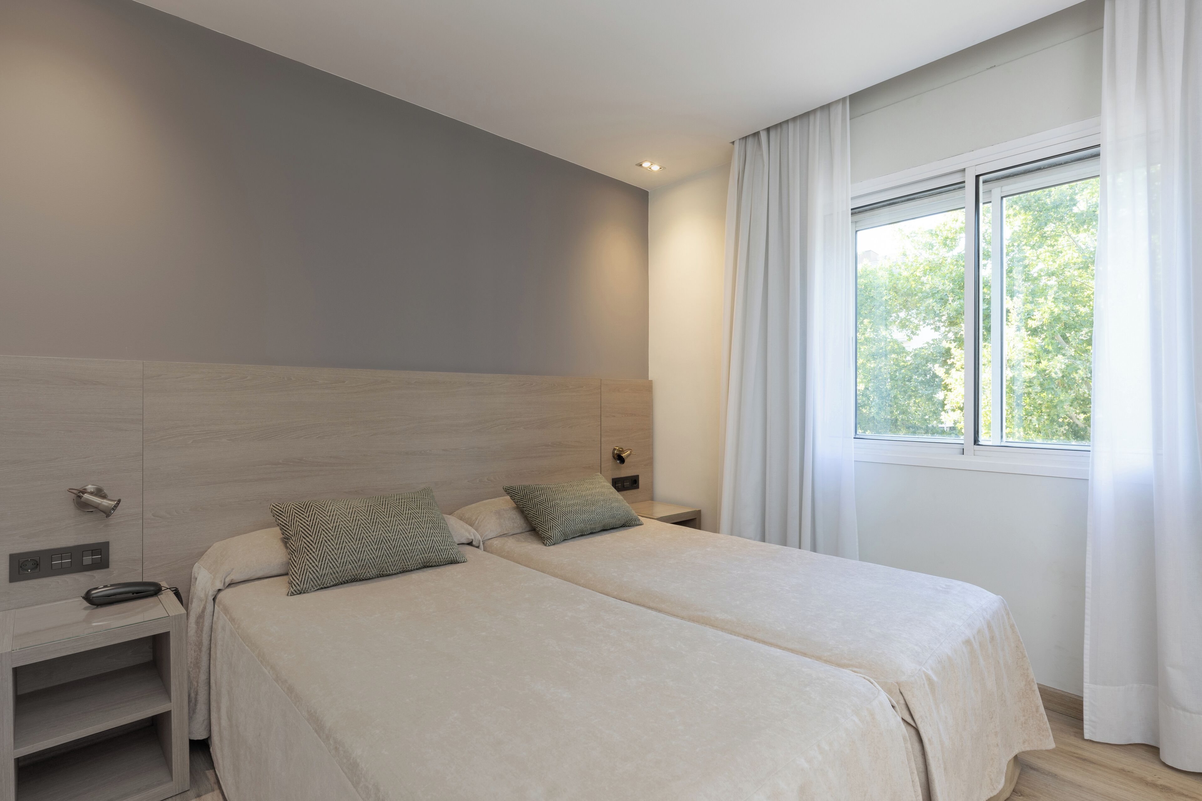 Un dormitorio moderno con dos camas, una mesita de noche y un ventanal con cortinas.