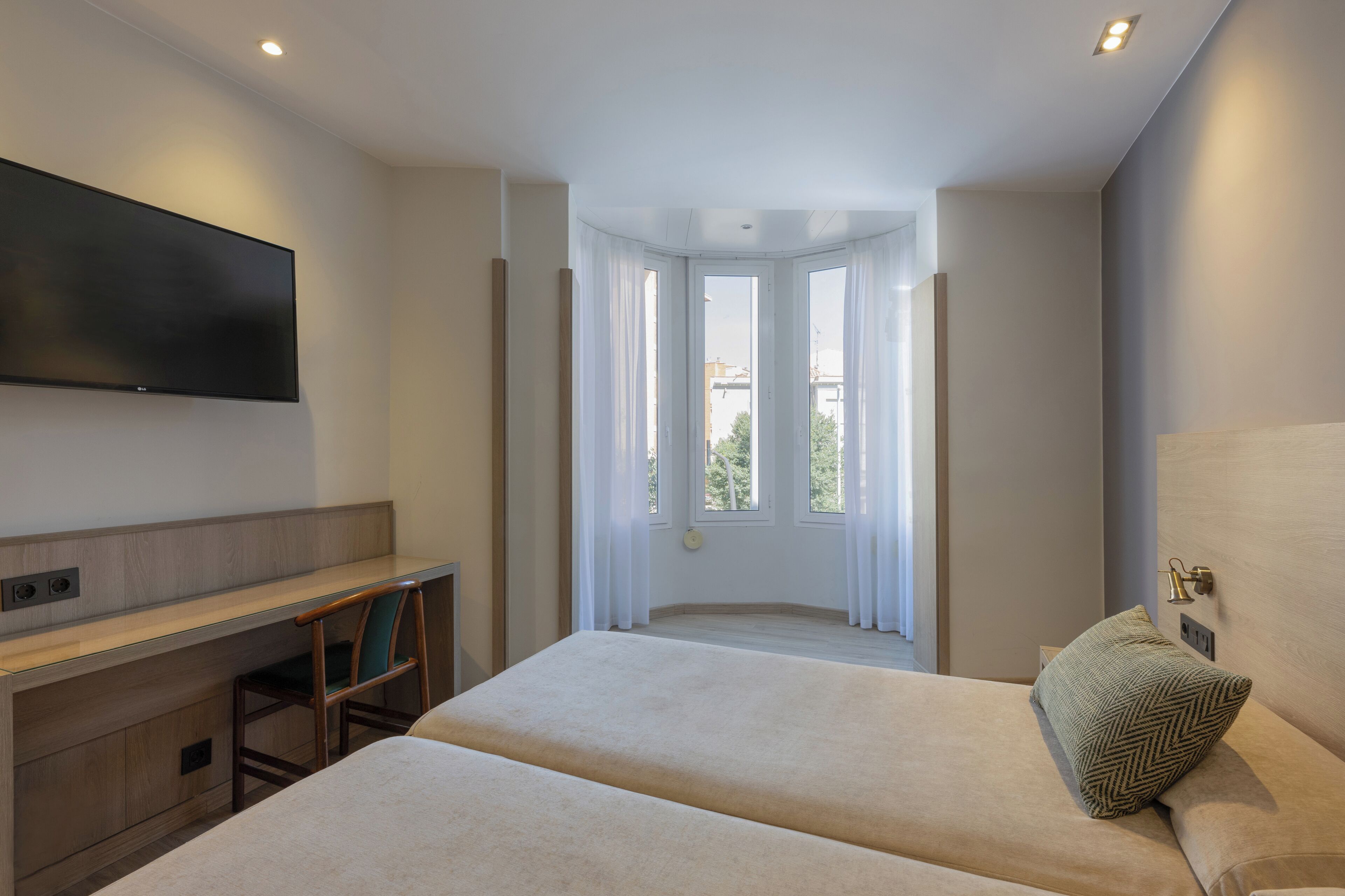 A modern hotel room with a large bed, a desk, and a TV mounted on the wall.
