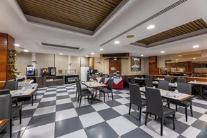 A restaurant with a checkered floor, tables with chairs, a counter with a coffee machine, and a wall with a painting. - Casanova Hotel (Fraga)