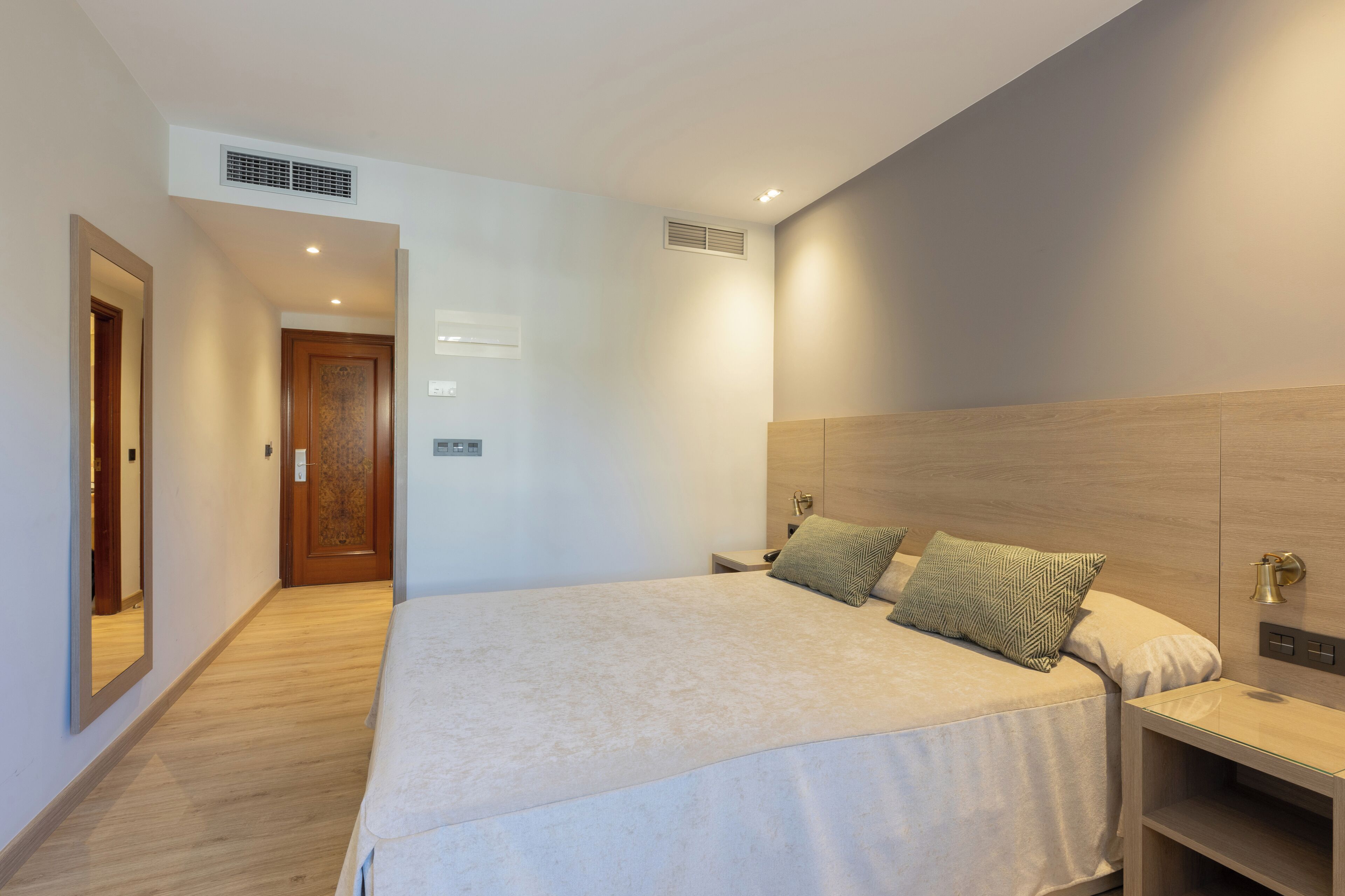 Een moderne hotelkamer met een groot bed, een houten hoofdbord, een nachtkastje en een spiegel.