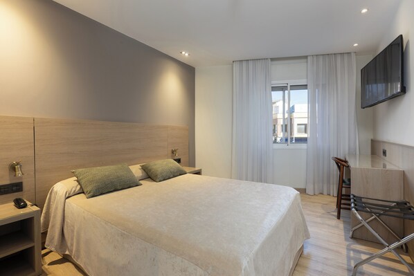 A modern hotel room with a large bed, a desk, a chair, a flat-screen TV, and a window with curtains. - Casanova Hotel (Fraga)