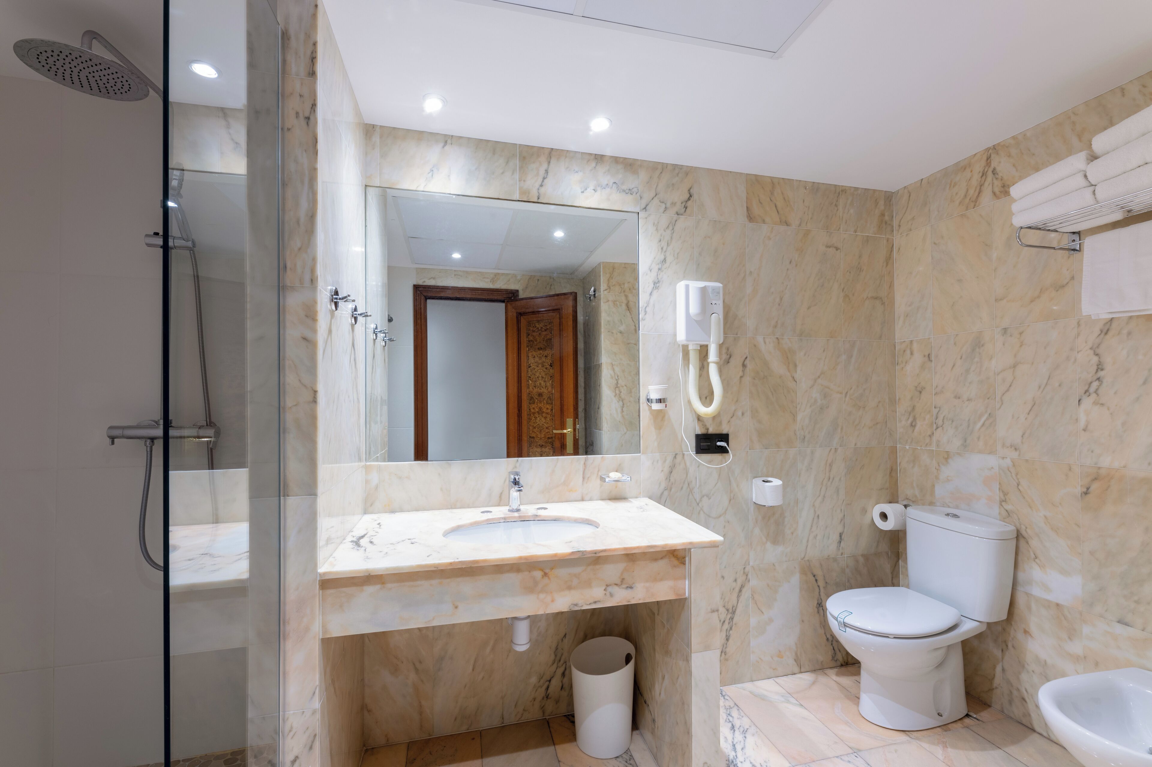 A modern bathroom with a glass-enclosed shower, a marble sink, a toilet, and a bidet.