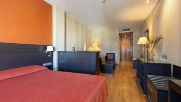 A hotel room with a bed, a desk, a chair, a lamp, and a small table.