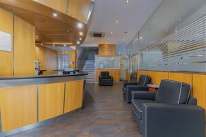 Zona de recepción con mostrador de madera, asientos y una escalera al fondo.