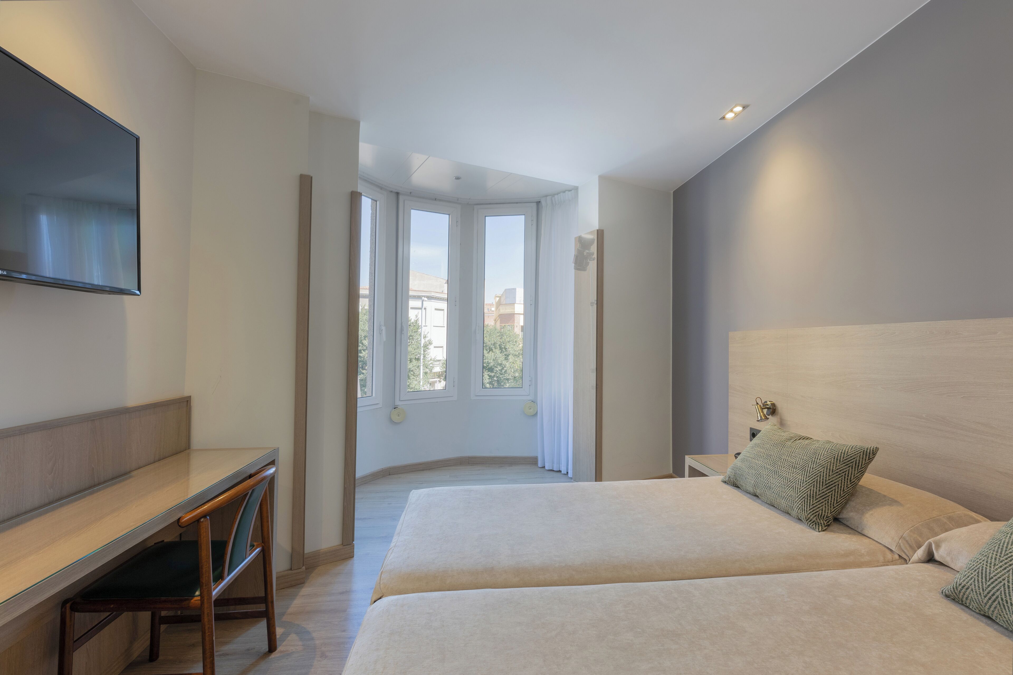 Une chambre d’hôtel moderne, dotée d’un bureau, de deux lits et d’une grande fenêtre donnant sur la ville.