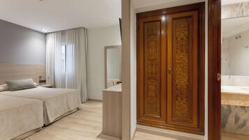 Habitación de hotel con dos camas, un armario de madera, un espejo y un baño con lavamanos de mármol.