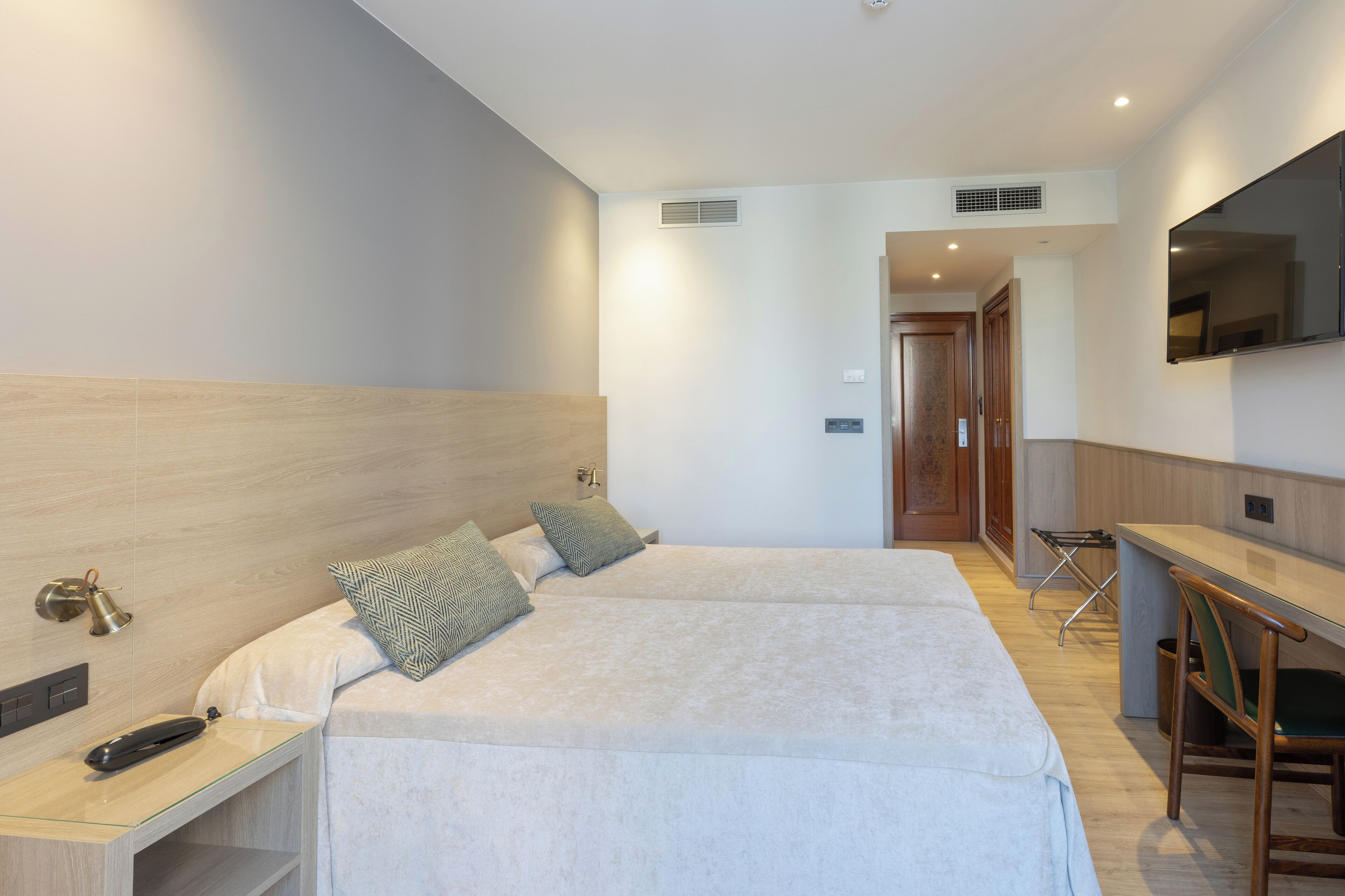 A hotel room with a bed, bedside table, and a desk with a chair.
