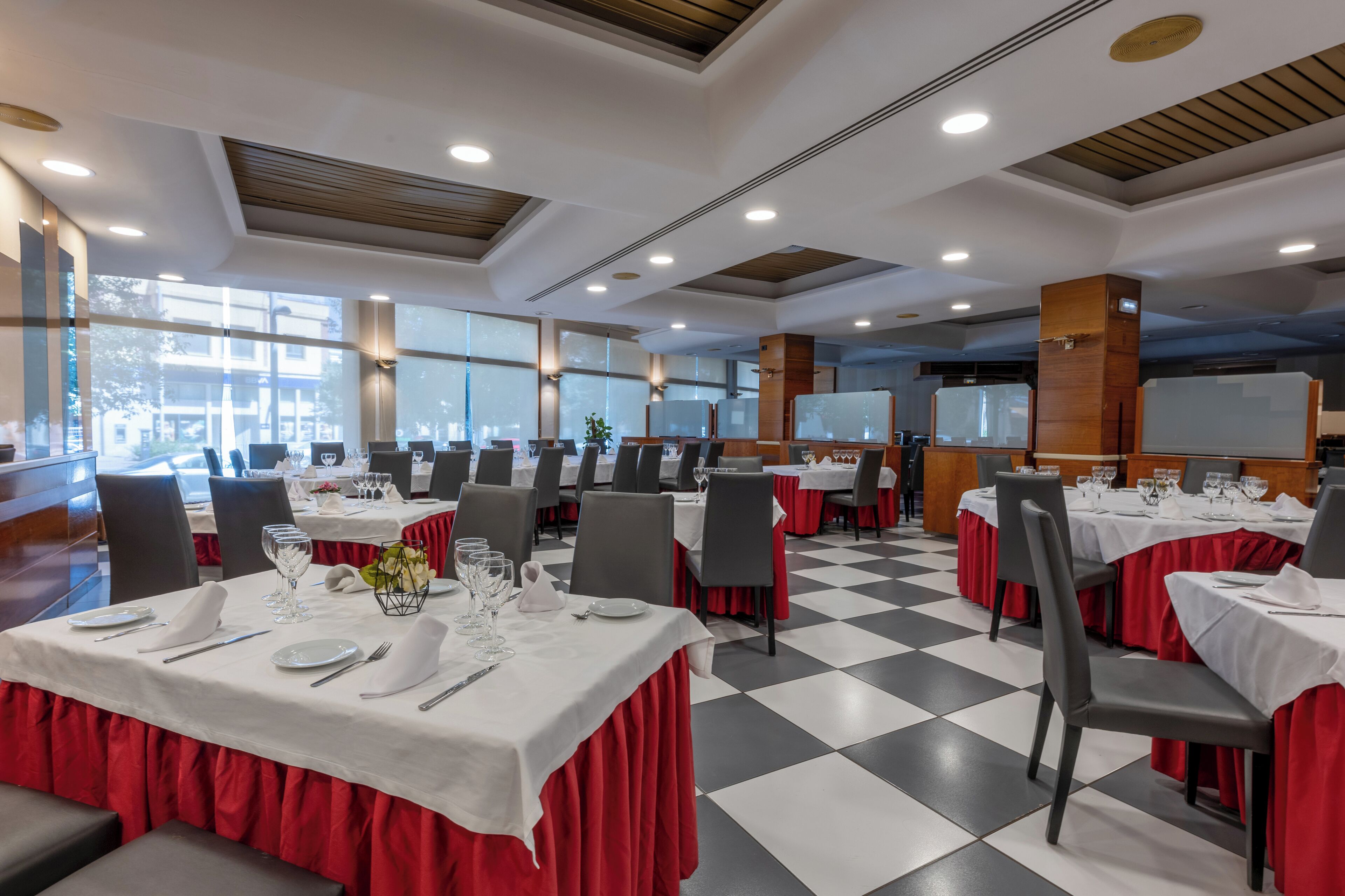Comedor con mesas dispuestas para el servicio, ventanas amplias y suelo a cuadros.