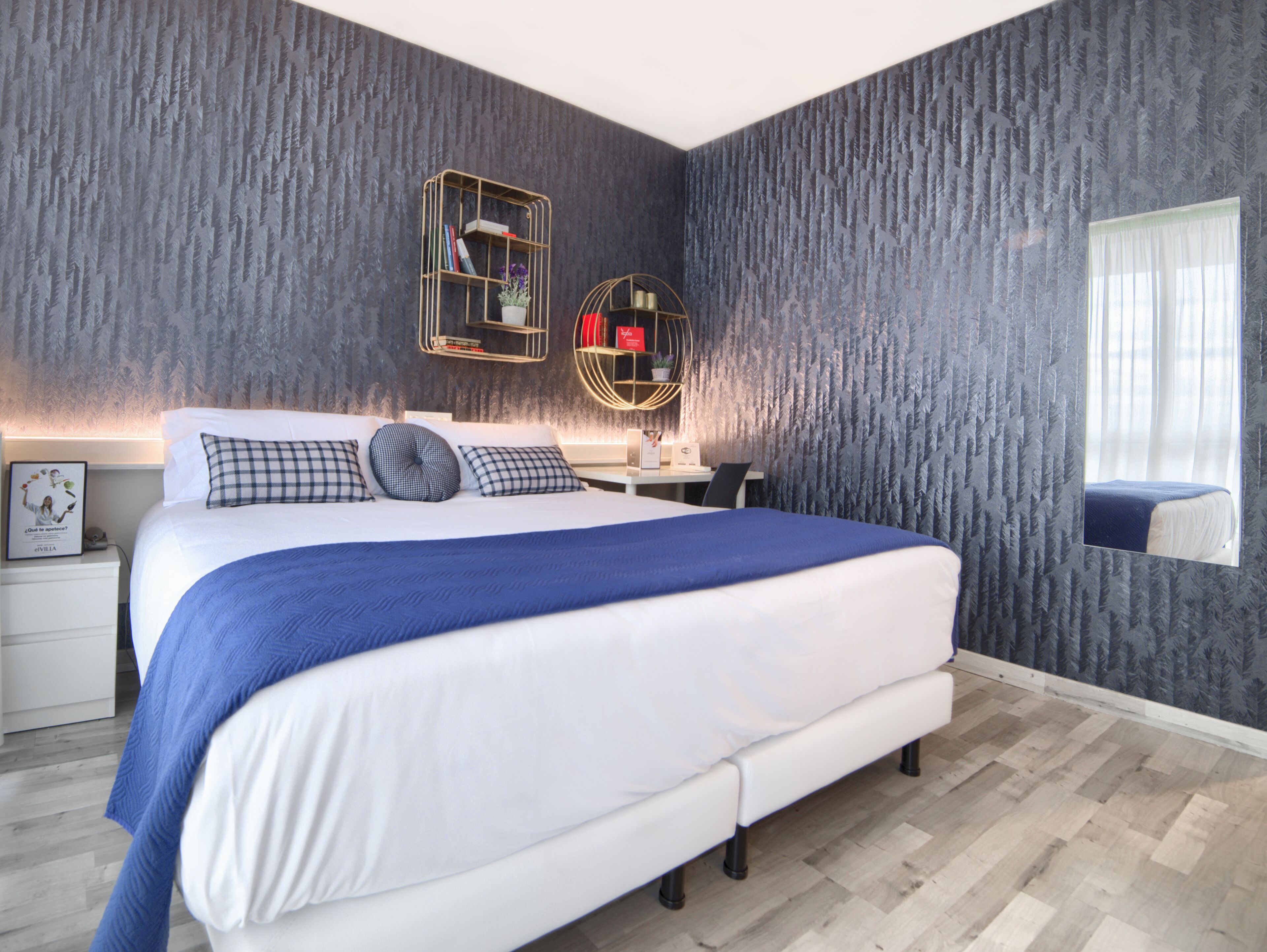 A modern bedroom with a large bed, a desk, and a mirror.