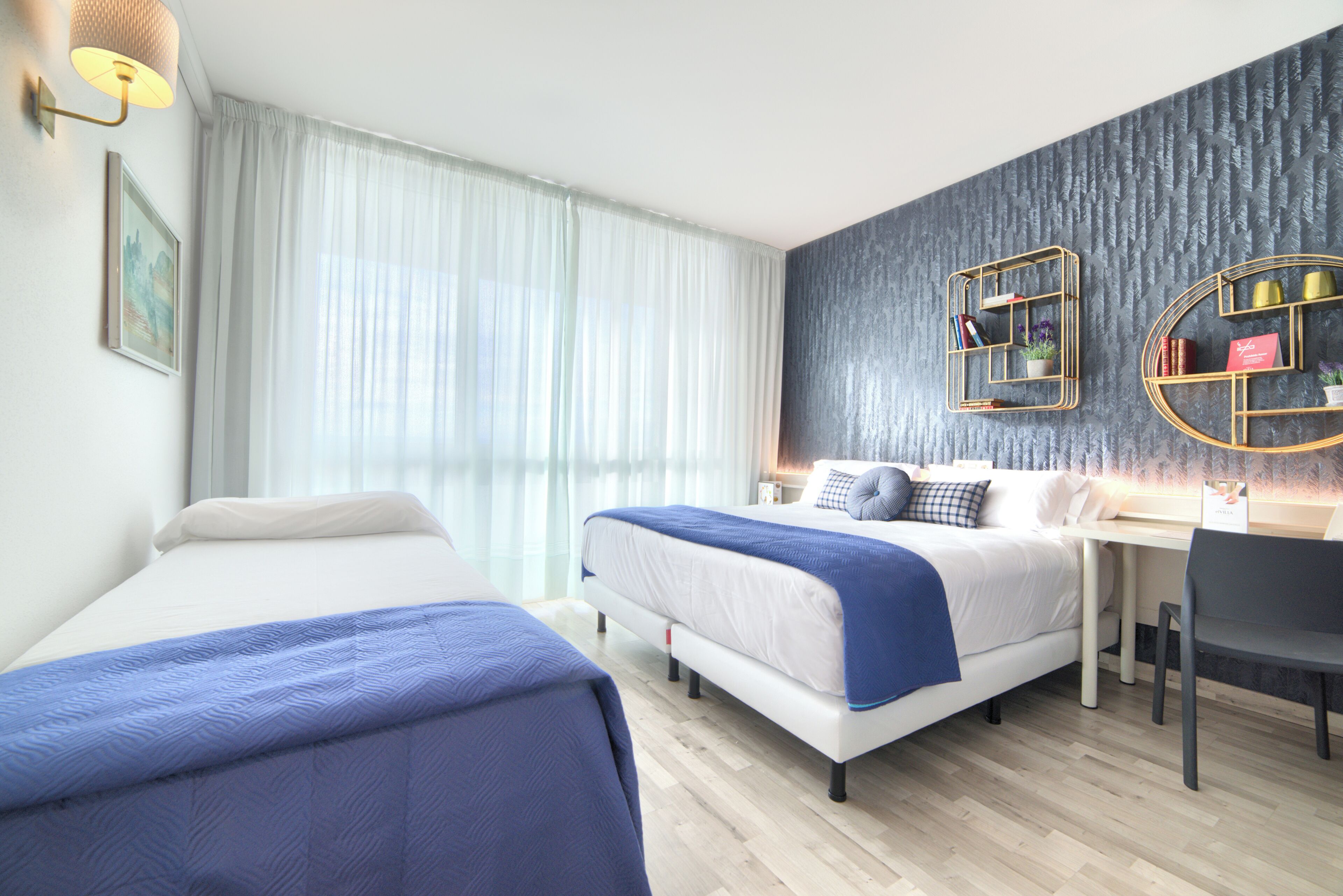 Una habitación de hotel moderna con dos camas, un escritorio y un gran ventanal con cortinas translúcidas.